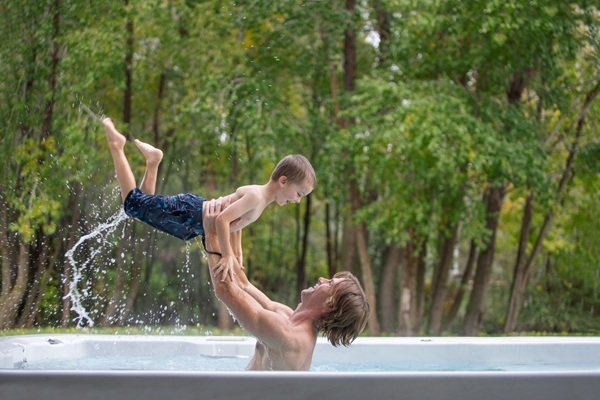 A man holding up a little boy while in a swim spa.